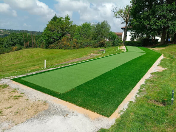 Outdoor tee line consisting of one continuous green synthetic grass strip surrounded by trees